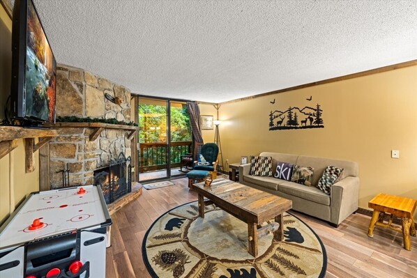 A cozy living room with a stone fireplace, a sofa, a coffee table, and a foosball table.