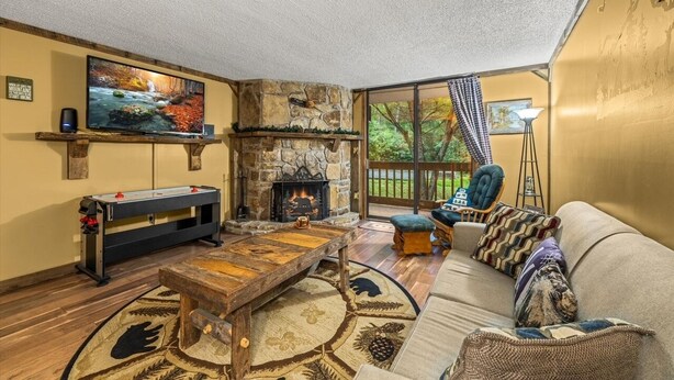 A cozy living room with a stone fireplace, a flat-screen TV, a foosball table, and a comfortable sofa. - Those Who Wander Are Not Always Lost – Cozy Mountain Stream Condo with Fireplace (Gatlinburg)