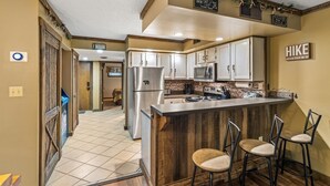 A compact kitchen with a central island, white cabinets, and a stainless steel refrigerator. - Those Who Wander Are Not Always Lost – Cozy Mountain Stream Condo with Fireplace (Gatlinburg)