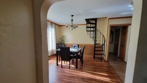 Una zona de menjador amb una taula i cadires, un penjoll i una escala que condueix a una altra habitació.