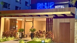 Ein Hotel mit modernem Design, das durch eine auffällige Neonreklame, einen überdachten Eingangsbereich und eine gepflegte Grünfläche gekennzeichnet ist.