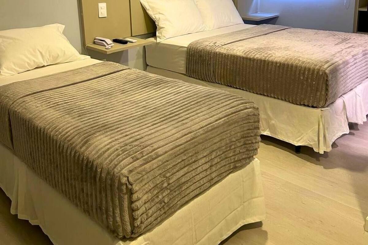 A hotel room with two beds, a bedside table with a phone, and a window with blinds.