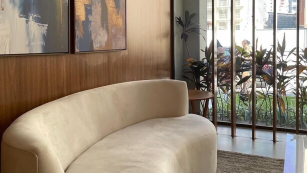 Ein modernes Wohnzimmer mit einer gebogenen Couch, abstrakter Wandkunst und einem großen Fenster mit Blick auf Grünflächen und Gebäude.