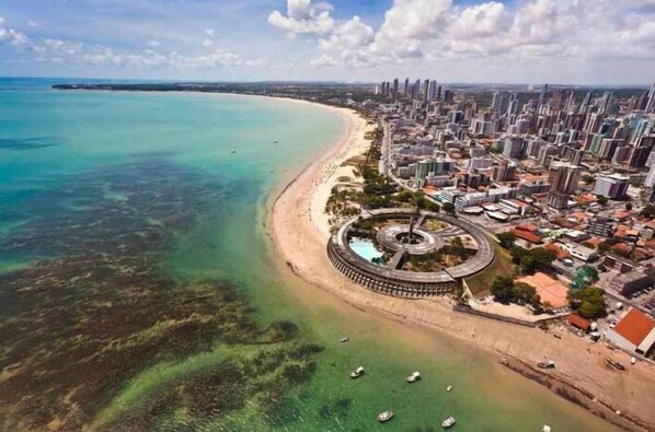 An aerial view of a coastal city with a beach, a roundabout, and high-rise buildings. - Blue Hotel (João Pessoa)