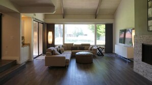 A spacious living room with a large sectional sofa, a round ottoman, and a fireplace. - Modern Mission Hills Country Club Townhome (Rancho Mirage)