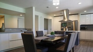 A modern kitchen with a central island, dark chairs, and a stainless steel range hood. - Modern Mission Hills Country Club Townhome (Rancho Mirage)