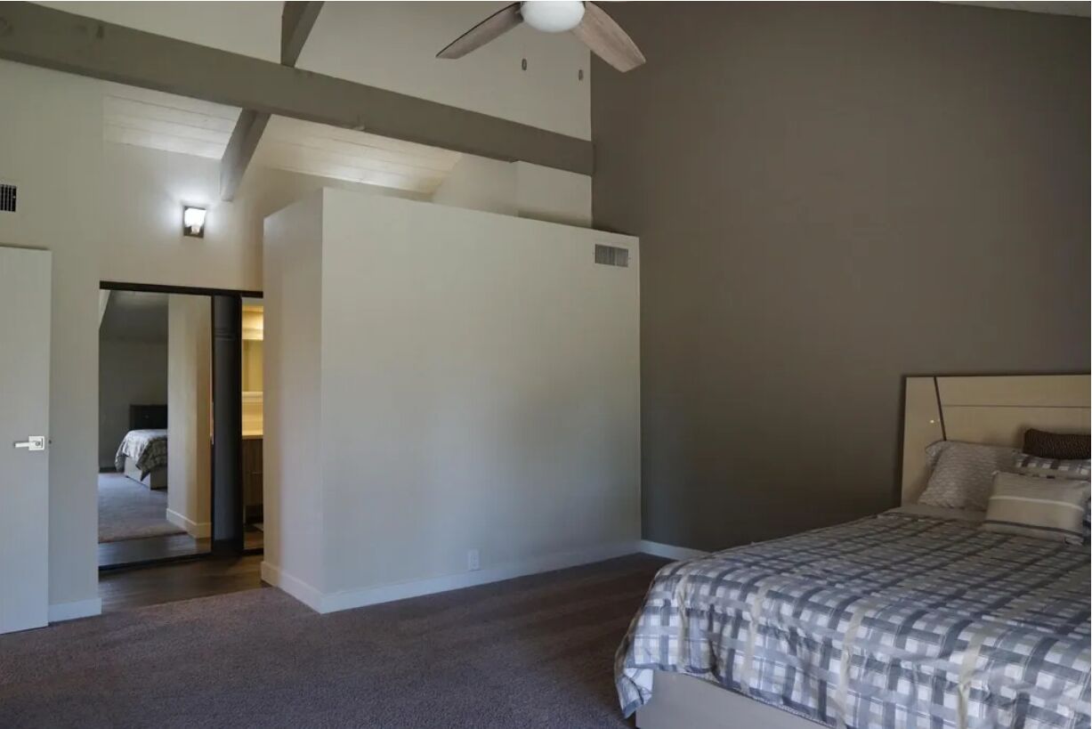 Une chambre à coucher avec un lit, un ventilateur de plafond et une porte donnant sur une autre pièce.