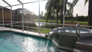Ein Pool mit Wasserfall, umgeben von einer Glaskonstruktion, mit Blick auf ein Haus und Palmen im Hintergrund.