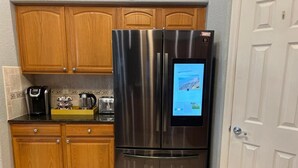 Ein Edelstahl-Kühlschrank mit digitaler Anzeige, Holzschränke und eine Kaffeemaschine auf der Arbeitsplatte.