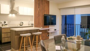 A modern kitchen with a central island, wooden accents, a flat-screen TV, and a balcony with a view. - Wynwood Residencial in Miraflores (Lima)