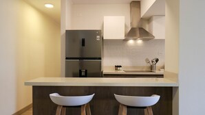 A modern kitchen with a stainless steel refrigerator, a double sink, and wooden bar stools. - Wynwood Residencial in Miraflores (Lima)