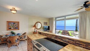 Eine Küche mit einer großen Kochinsel, ein Essbereich mit Korbstühlen, einem Fernseher und Blick auf den Ozean.