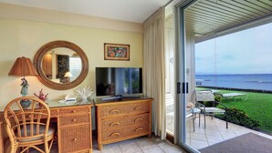 Ein Zimmer mit Fernseher, Korbmöbeln, einem Spiegel und Meerblick.