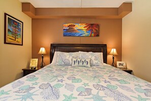 Habitación de hotel con cama, una colcha con motivos marinos, una mesita de noche con lámpara, un cartel enmarcado en la pared y un cuadro sobre la cama.