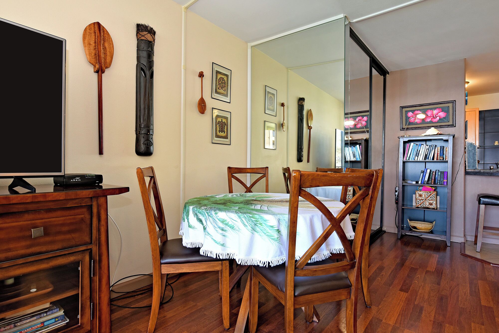 A dining area with a wooden table, chairs, a television, and a bookshelf.