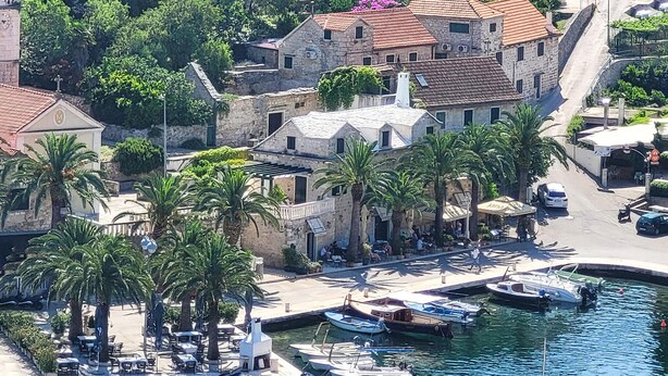 A coastal town with stone buildings, a marina with small boats, and palm trees along the waterfront.