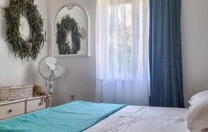 Camera da letto con un letto, una ventola, una finestra con tende leggere e due ghirlande appese al muro.