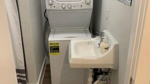 A compact laundry room with a washing machine, a sink, and a small rug on the floor. - The Private Place- unit 1 (Alvin)