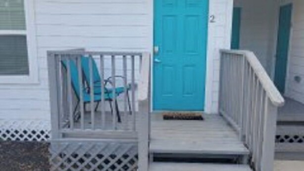 A single-story house with a blue door and a small porch with a chair. - The Private Place- unit 1 (Alvin)