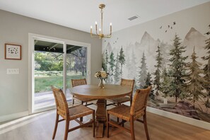 Enjoy meals in this cozy dining area with a round table and four chairs, surrounded by a beautiful mural and a window with a view.