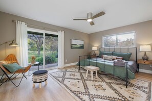 Relax in a cozy seating area with a comfortable chair and ottoman, a neatly made bed, and a large window offering a view of the outdoors.