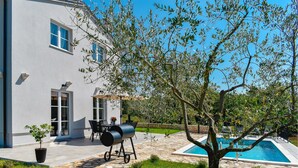 Une maison moderne dotée d’une piscine, d’un espace salon extérieur et d’un coin barbecue.
