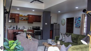 A modern living room with a grey sofa, a green sofa, and a coffee table. There is a kitchen in the background with wooden cabinets and appliances. - Villa Torre II (Belize City)