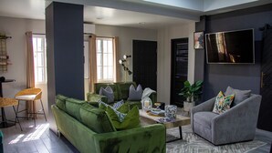 A modern living room with a green sofa, a grey armchair, and a coffee table. There is a TV mounted on the wall and a window with curtains. - Villa Torre II (Belize City)