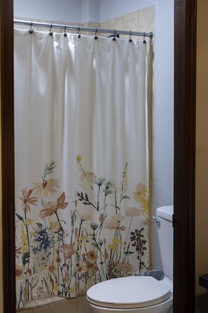 Ein Badezimmer mit Toilette, einer Duschvorhang mit Blumenmuster und einem Handtuch an der Wand.