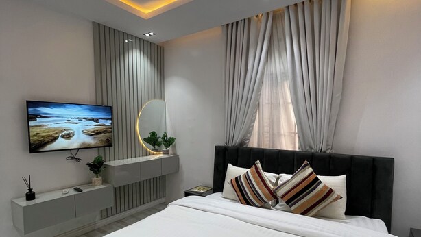 Ein modernes Schlafzimmer mit einem großen Bett, einem an der Wand montierten Fernseher, einem Nachttisch und einer Deckenleuchte.