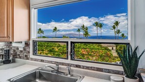 Una cocina con un amplio ventanal que ofrece una vista panorámica de palmeras y el océano.