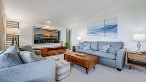 Una sala de estar moderna con un sofá gris, una mesa de centro de madera y un cuadro grande de una puesta de sol.