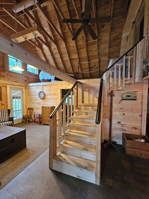 Een houten chalet van binnen, met een trap naar een slaapzolder, een eettafel en een klok aan de muur.