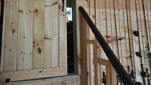 A wooden staircase leading to a room with a large wooden door and fishing rods mounted on the wall. - Spacious cabin on beautiful Long Lake w/waterfront view, private dock, fire pit. (Princeton)