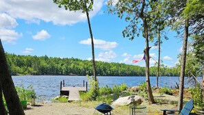 A lakeside campsite with a dock, a picnic table, and two Adirondack chairs. - Spacious cabin on beautiful Long Lake w/waterfront view, private dock, fire pit. (Princeton)