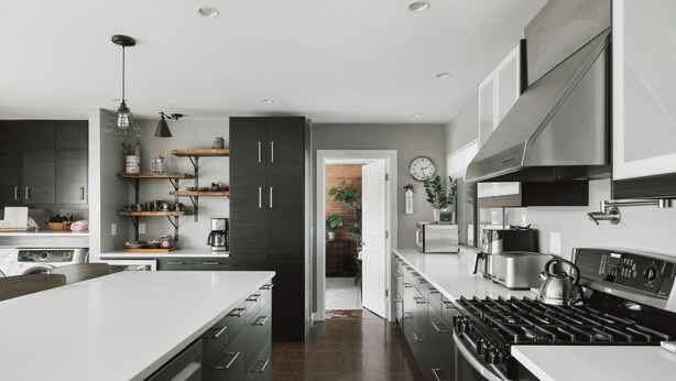 Une cuisine moderne avec des meubles de couleur sombre, un grand îlot central, des appareils électroménagers en acier inoxydable et une porte visible donnant sur une autre pièce.