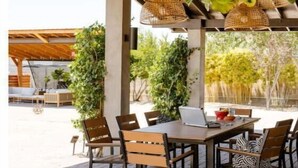 Une terrasse extérieure avec une table et des chaises en bois, entourée de verdure et agrémentée de lampes en osier suspendues.