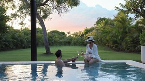 A couple in a private pool with a lush garden and a sunset in the background.