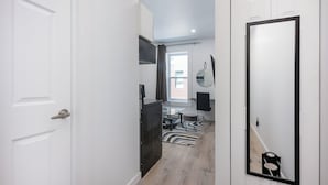 A hallway with a white door, a black-framed mirror, a dining area with a table and chairs, and a window with curtains.
