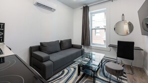 A modern living room with a grey sofa, a glass coffee table, a round mirror, and a window with curtains.