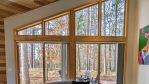 A modern living room with a large window, a sofa, a coffee table, and two armchairs. - Deer Cabin @ Orange Tractor Retreat: a new, 3BR modern cabin on 40 private acres (Wisconsin Dells)
