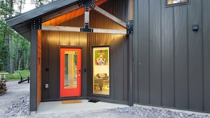 A modern cabin with a red door, wooden exterior, and a cozy interior visible through the glass door. - Deer Cabin @ Orange Tractor Retreat: a new, 3BR modern cabin on 40 private acres (Wisconsin Dells)