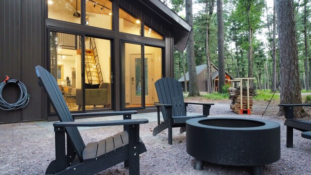 A cabin with a large glass door, outdoor seating, and a fire pit. - Deer Cabin @ Orange Tractor Retreat: a new, 3BR modern cabin on 40 private acres (Wisconsin Dells)