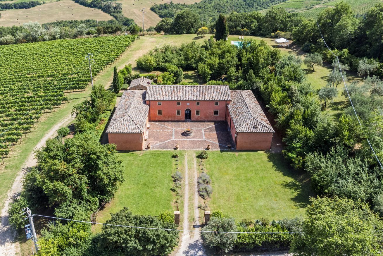 Un grand bâtiment doté d’une cour intérieure, entouré d’une végétation luxuriante et de vignobles.