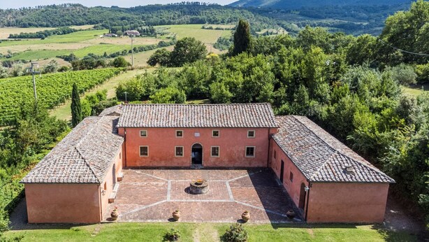 A large, rectangular building with a tiled roof, surrounded by a well-maintained lawn and a vineyard in the background. - Villa Boschetto By MMega (Montepulciano)