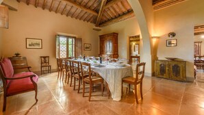 A dining room with a long table set for a meal, wooden chairs, a red chair, and a cabinet with a mirror. - Villa Boschetto By MMega (Montepulciano)