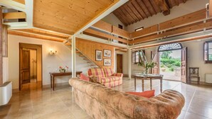 A spacious living area with a high ceiling, wooden beams, a large sofa, a coffee table, and a staircase leading to an upper level. - Villa Boschetto By MMega (Montepulciano)