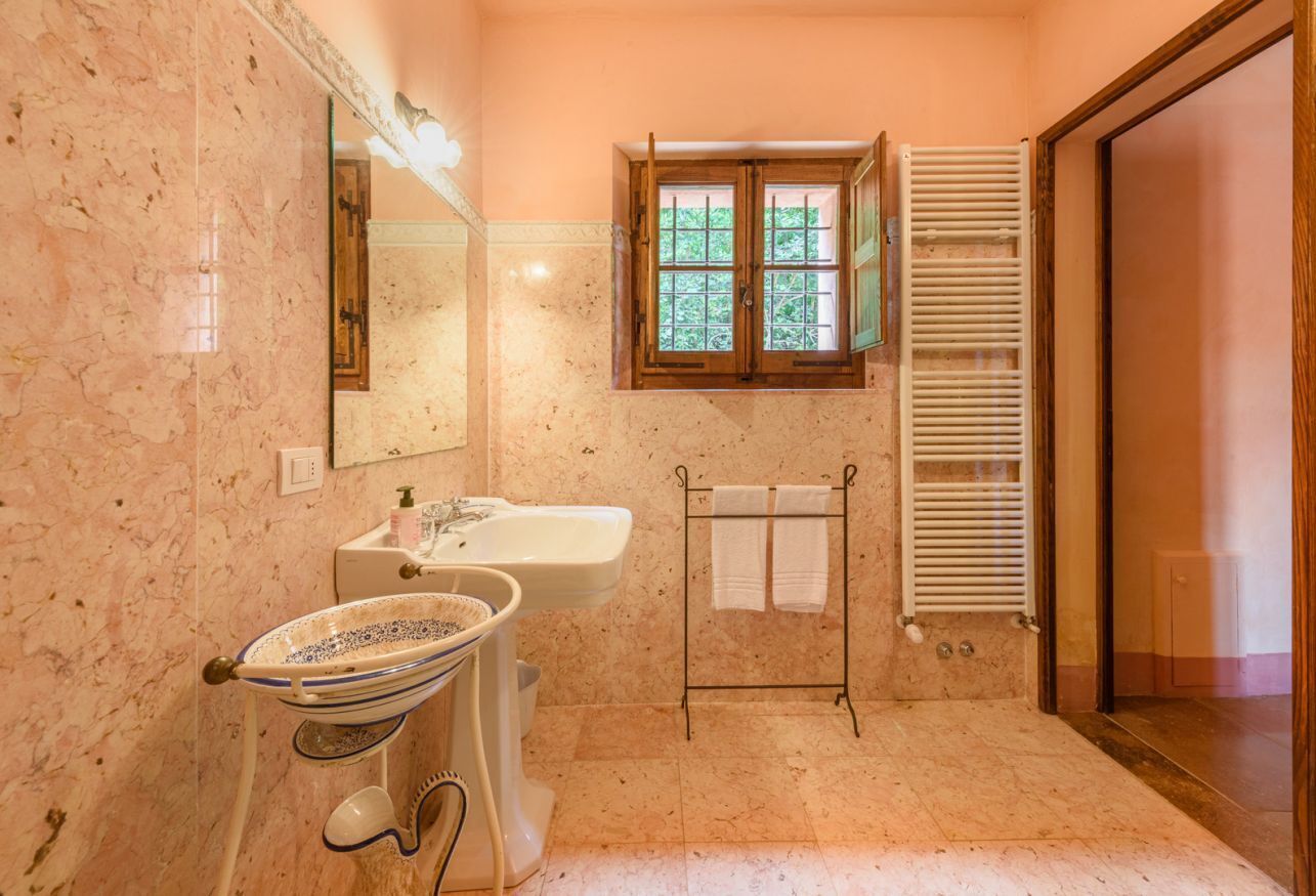 A bathroom with a marble sink, a mirror, a window with shutters, and a towel rack.