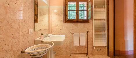 A bathroom with a marble sink, a mirror, a window with shutters, and a towel rack.