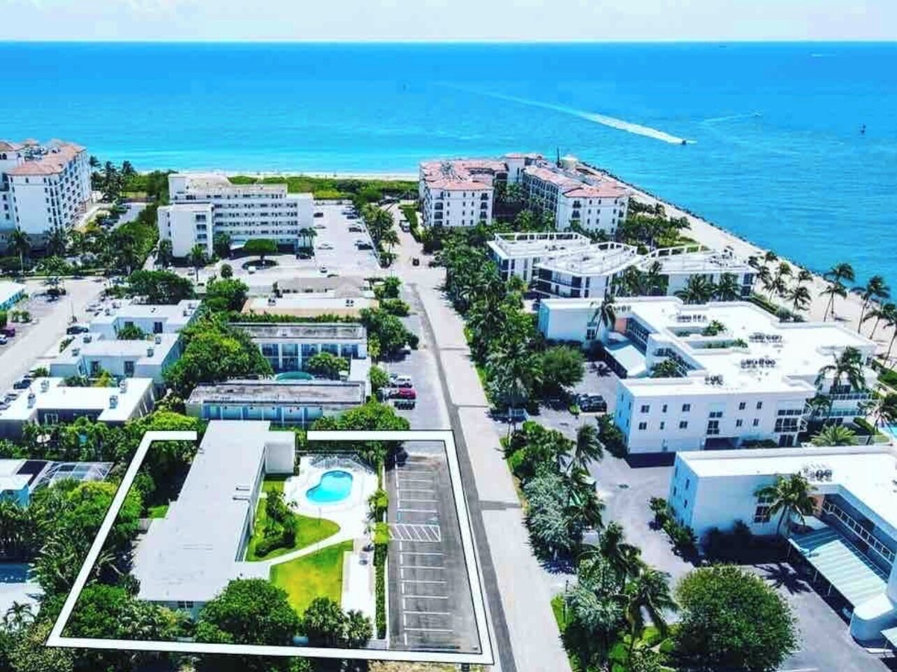 An aerial view of a coastal hotel complex with multiple buildings, a parking lot, and a swimming pool.
